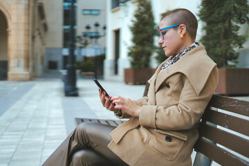 A fashionable young woman is deeply engaged with her smartphone in an urban environment