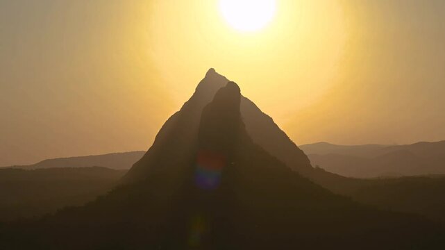 Aerial view of majestic Mt Beerwah and Mt Coonowrin under a tranquil orange sky at dusk, Glass House Mountains, Queensland, Australia.