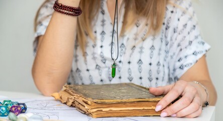 A female fortune teller reads a book of spells and a pendulum above the book.