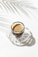 A cup of coffee on white background with palm tree leaf shadow. Minimal style