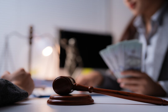 Judge's gavel lying on the table during a bribery, lawyer receiving money from client in the office in the background, corruption and venality concept