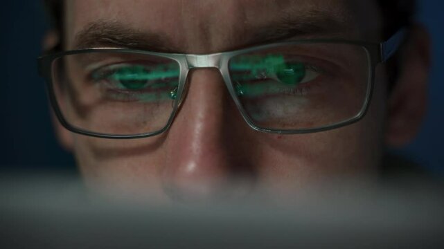 Close-up of a focused coder with glasses, writing a script. Programming code reflecting on developers eyeglasses 