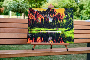 A vibrant painting displayed outdoors, placed on an easel amidst a beautiful natural landscape,...