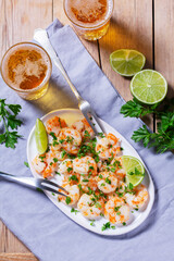 Shrimp cooked with garlic and herbs, served with beer and lime on a wooden table.
