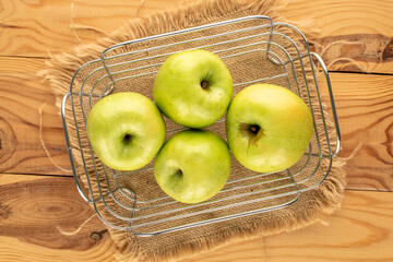Several sweet green apples in a basket on a wooden table, close-up, top view.
