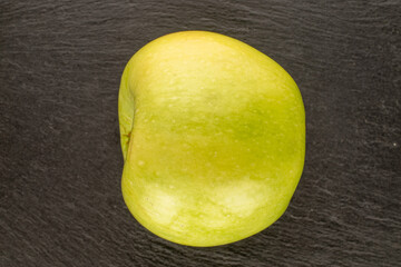 One sweet green apple on slate stone, macro, top view.