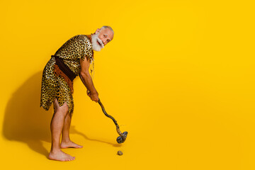 Photo of crazy caveman playing golf with rock club hitting isolated over yellow color background