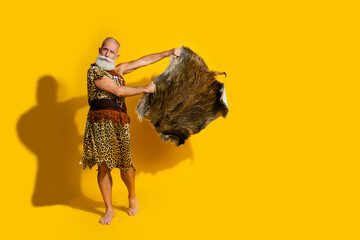 Full size photo of ancient aged caveman leopard skin clothes hold animal fur empty space isolated on yellow color background