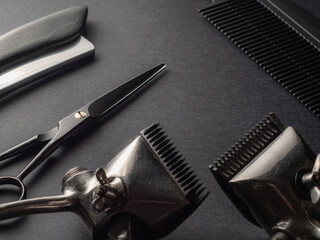 Various grooming tools including clippers, scissors, and a comb are arranged on a dark surface, showcasing the essentials for hair cutting in a barbershop environment