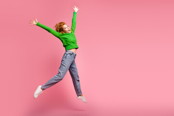 Young woman celebrating joyfully while jumping on vibrant pink background wearing a green sweater...