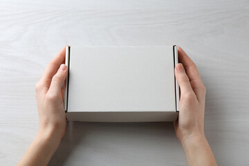 Woman with blank cardboard box on white wooden background, closeup. Mockup for design