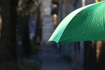Open green umbrella under pouring rain outdoors, closeup. Space for text