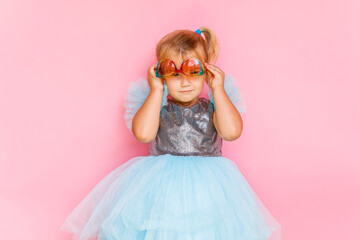 Girl with long hair in festive paper hat and dressy dress on pink background tossing gold confetti