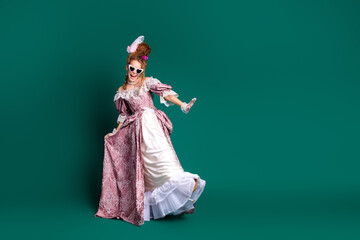 Joyful young woman in pink baroque dress posing against green background, blending historic elegance with modern flair