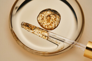 24 k gold facial serum in a pipette on a gold background.