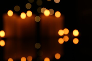 Fototapeta premium Blurred view of burning candles in darkness, bokeh effect