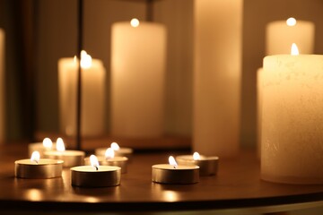 Many burning candles on wooden table, closeup