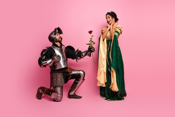 Medieval-themed couple moment with elaborate costumes in front of a pink background