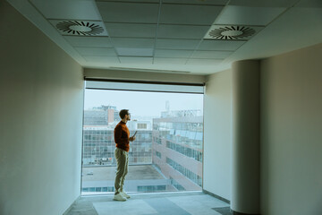 Fototapeta premium Man enjoying a quiet moment while gazing out of a large window in a modern building