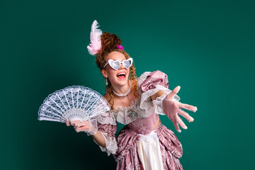 Young woman in baroque costume with lace fan on green background showcasing retro glamour and...