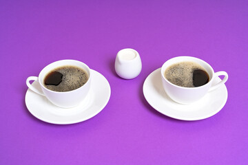 Two Cups of Black Coffee with a Milk Jug on a Purple Background