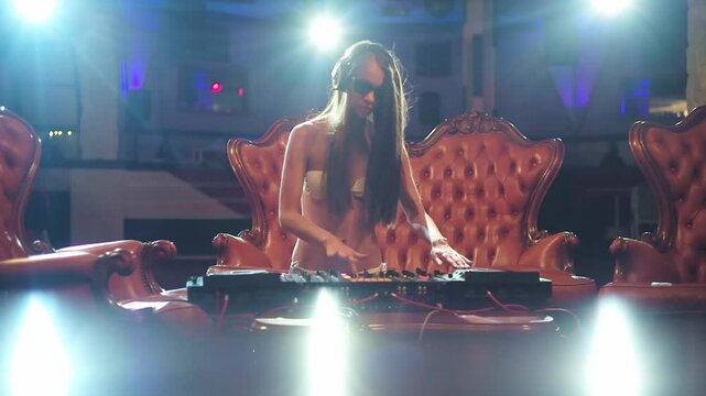 Sexy woman Dj mixing music at the club. Glamorous female DJ. Sexy Dj enjoying nightlife. Sexy clubbing girl with a headset. Sensual woman dancing to electronic music. Luxury nightclub scene with a DJ.