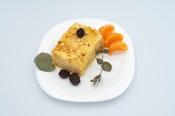 A piece of Napoleon cake with blackberries on a white plate. Dessert.