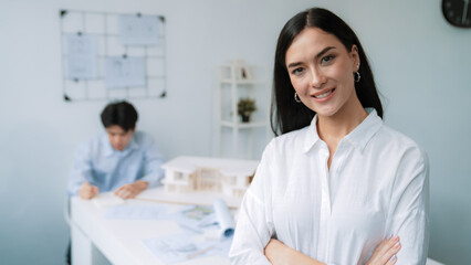 Closeup of female professional architect engineer cross arms with confident while skilled coworker focus on drawing blueprint at table with house model. Creative living and design concept. Immaculate.