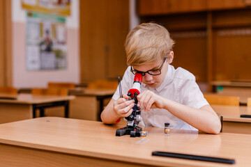 8-year-old smart schoolboy in glasses studying through a microscope at school