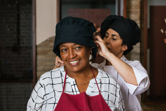 Professional chef helping trainee wearing chef hat in restaurant kitchen - Powered by Adobe