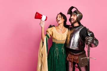 Playful couple in medieval costumes posing against a pink backdrop