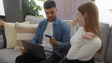 Couple at home celebrates online purchase with card, man with laptop and woman hugging joyfully in cozy living room.