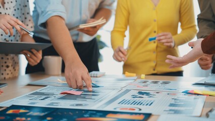 Fototapeta premium A dynamic group of professionals collaborates in a bright office space. They analyze various graphs and charts while discussing strategies using sticky notes and documents. SACTR