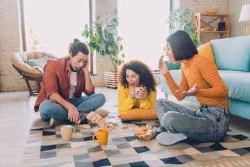 Three young friends enjoying a fun time playing a game with blocks while relaxing together in a...
