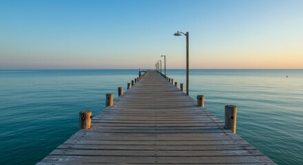 Fototapeta premium Serene Ocean Pier at Dawn - Tranquil sunrise view of a long wooden pier extending into calm, turquoise ocean water. Peaceful and idyllic scene
