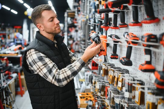 Portrait of young bearded man buying modern electric drill while standing in tool. Hardware construction site objects concept