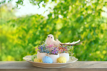 cute easter decoration with bird toy and flowers in eggs shells outdoor, nature background. festive composition for Easter holiday, spring season.