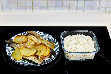 A plate of fish with potatoes next to a bowl of rice