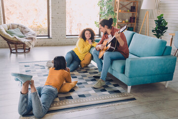 Group of young friends enjoying leisure time at home together with music, conversation, and joyful...