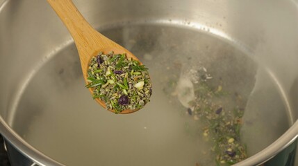 Wooden spoon with green herbs, including parsley and basil, floating in large shallow metal pot. Fresh green tones and natural textures inspire flavorful, healthy cooking and aromatic meals.