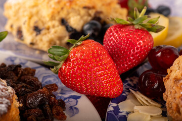 A plate of food with a strawberry on it. The plate is blue and white. There are other fruits and pastries on the plate