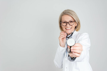 Smiling happy doctor pointing with stethoscope to camera on grey background.