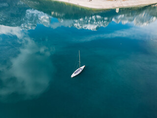 Fototapeta premium Aerial drone view of Lake Molveno, beautiful lake in Italy. Lake in dolomites from drone in winter. Lake Molveno in Italy. Sailboat, yacht on crystal clear lake in the Brenta Dolomites