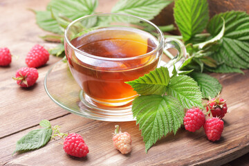 Raspberry leaf tea in glass cup with leaves and berry on rustic background, natural green medicine for menopause, pms, pregnancy, woman drink concept