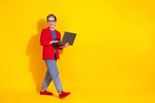 Stylish mature woman in colorful outfit holding a laptop against a vibrant yellow background expressing positivity