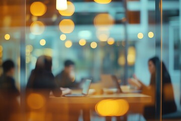 blurred photo of an office meeting room with business people sitting around the table with laptops and documents, discussing business plans, talking and working together