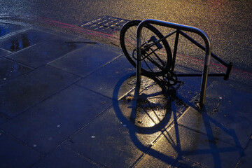 Rear wheel of a bike chained to metal pipe at night street, other parts already stolen