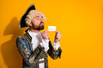 Elegant nobleman in vintage attire holding a credit card against yellow background expressing...