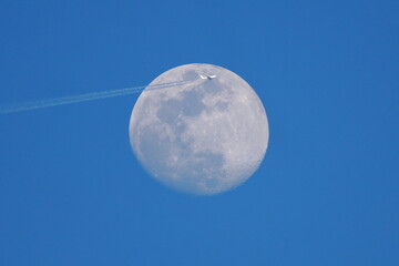 Plane commercial jet flies past a full moon. 