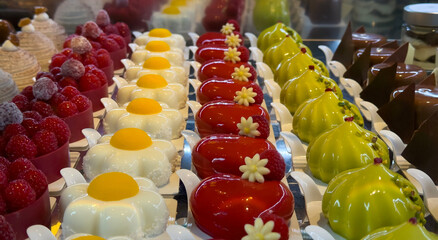 Delicious mix of different mini cakes displayed in a pastry shop. Colored desserts